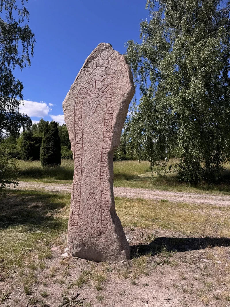 A tall runestone with red-painted runic inscriptions standing in a grassy field