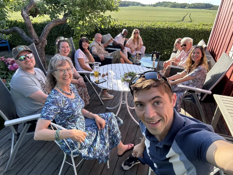 Group selfie with about ten people on a wooden deck with countryside view