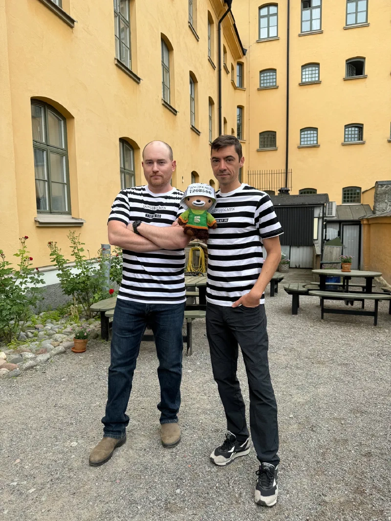 Adam and Nicholas in striped prisoner shirts with Sumi in a prisoner cap in the courtyard