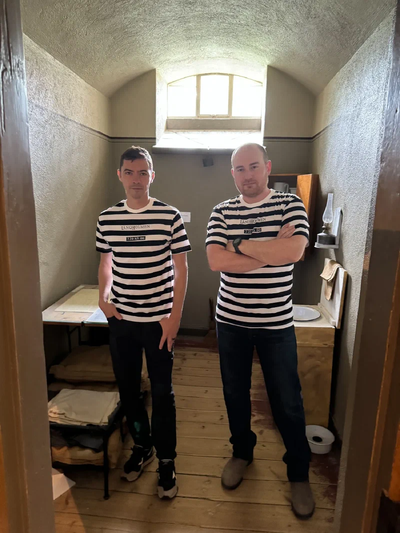 Nicholas and Adam in prisoner shirts inside a preserved prison cell
