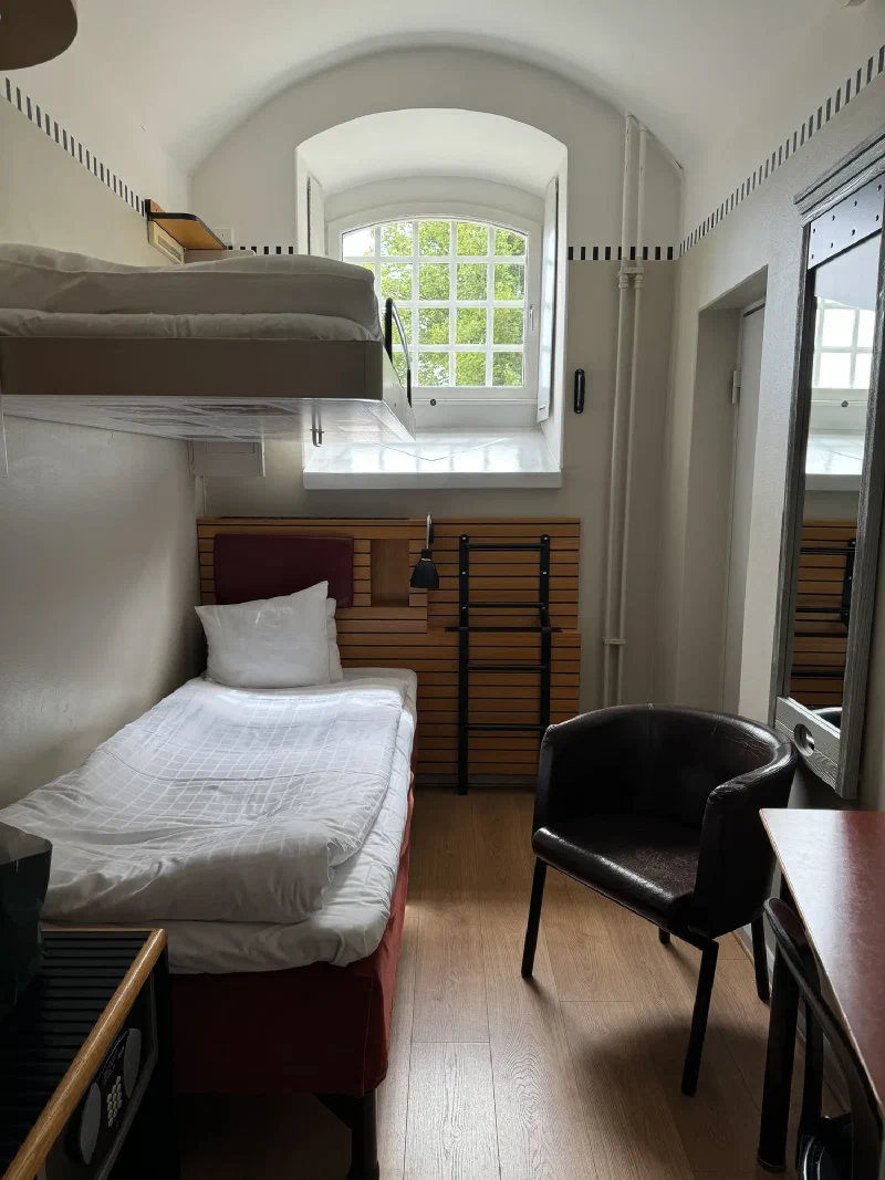 Narrow prison cell converted to hotel room with bunk beds and arched window