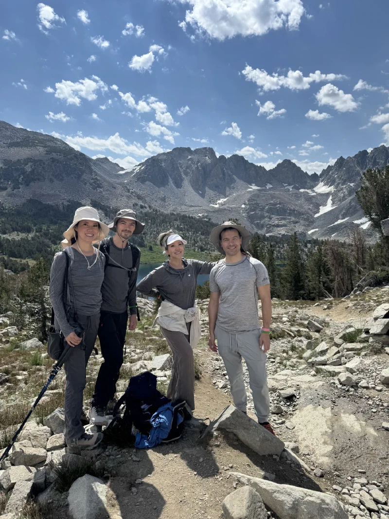Four hikers posing on a rocky trail above a blue alpine lake