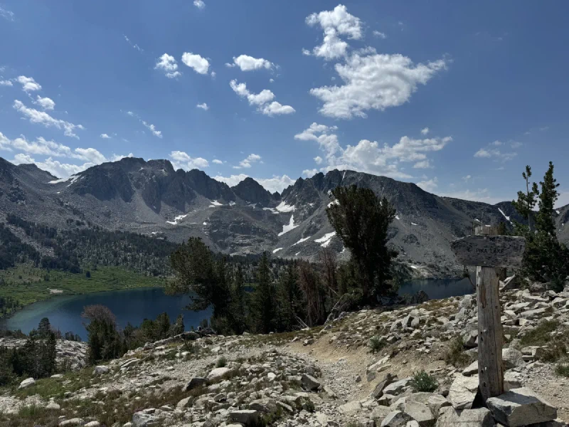Hiking trail with wooden sign reading Pika Lake and arrow, mountain scenery beyond