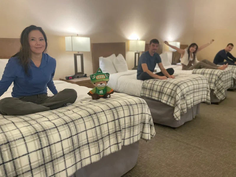Five travelers sitting on four twin beds lined up in a row in a hotel loft