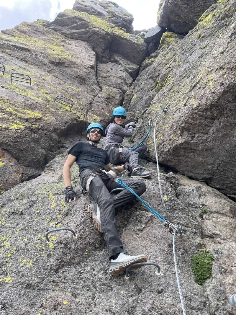 Two climbers resting on a rock face while clipped into via ferrata cables
