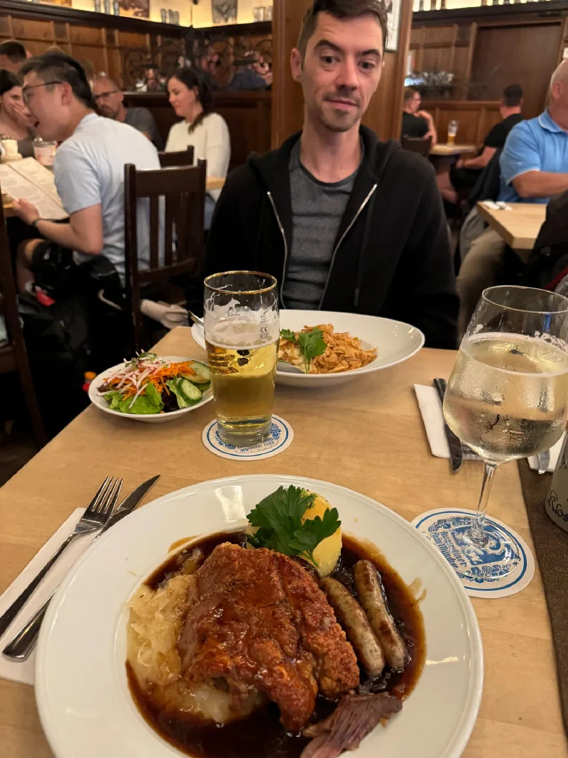 Nicholas seated at a traditional Bavarian restaurant table with German food and beer