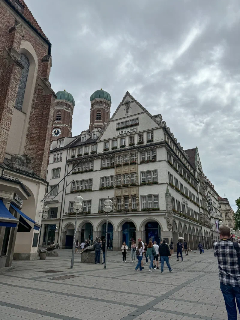 HIRMER building in Munich with Frauenkirche twin domes behind it under cloudy sky