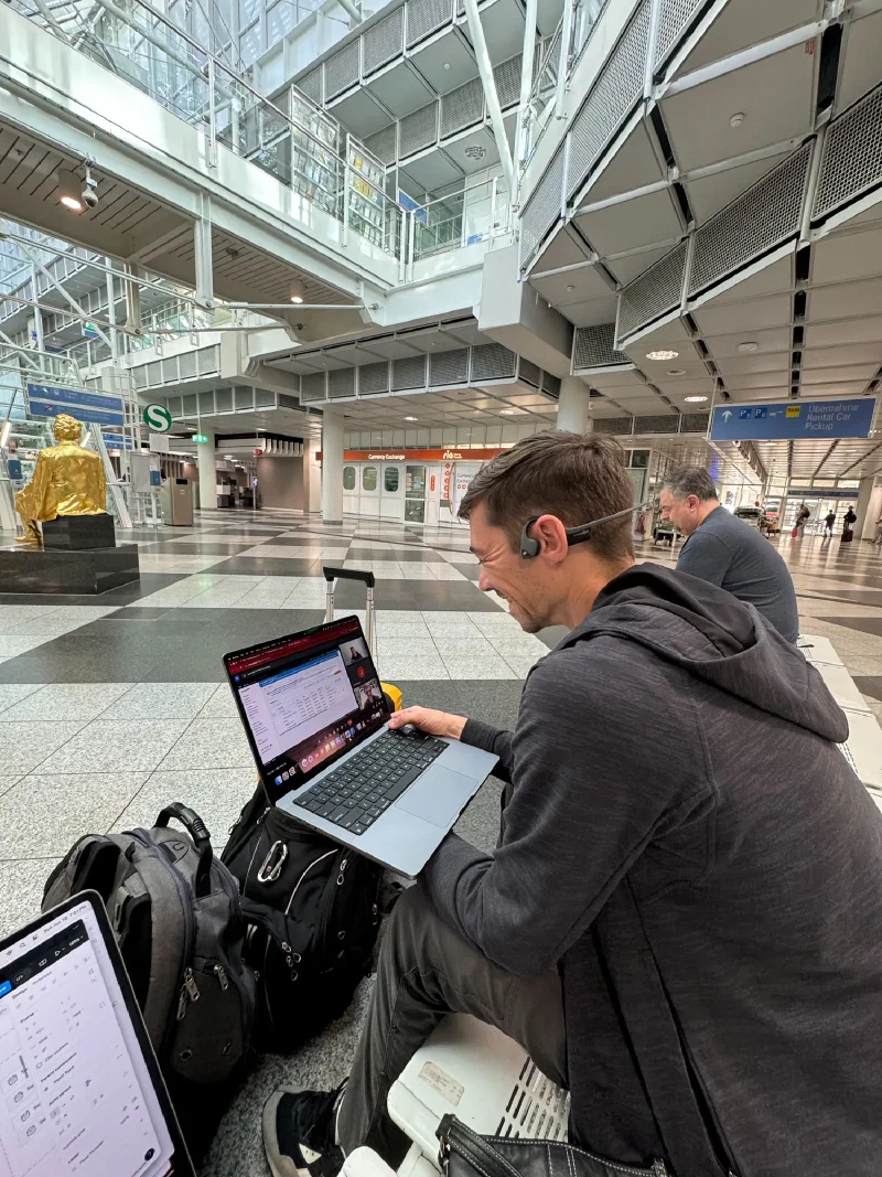 Nicholas on a work call with laptop and luggage at Munich Airport