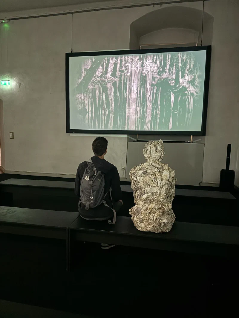 Nicholas watching a black and white video projection with eerie sculpture