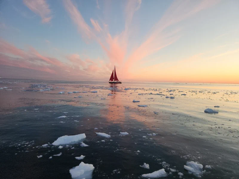 Red sailboat among icebergs at sunset in Greenland
