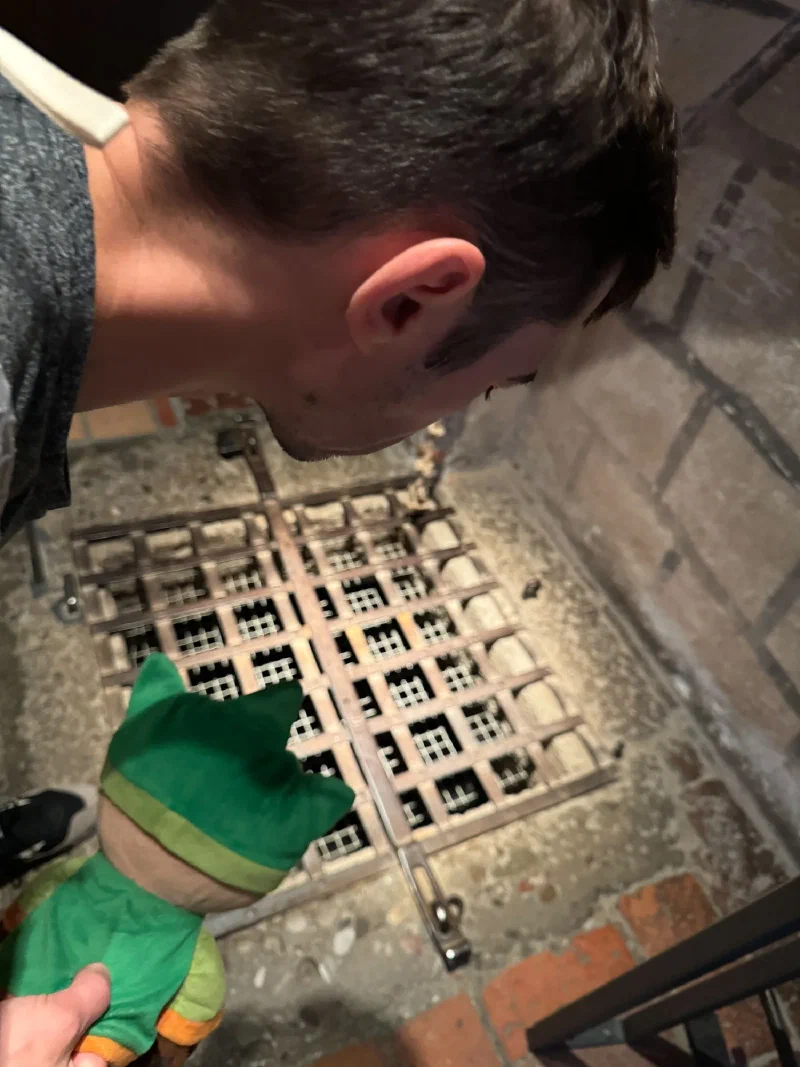 Nicholas and Sumi peering down through a murder hole with iron grate inside the fortress