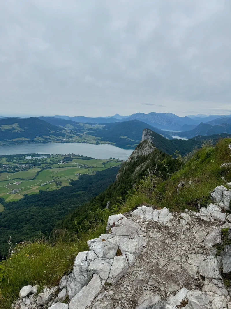 Summit panorama with lake, dramatic cliff face, and patchwork fields below