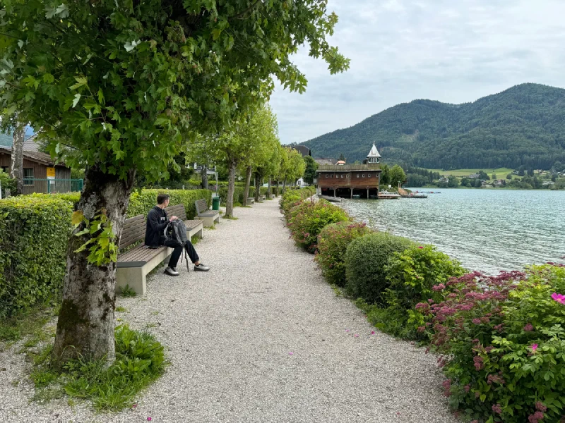 Nicholas settling onto a lakeside bench with backpack
