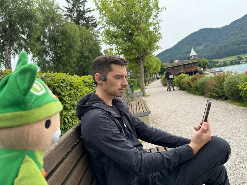 Nicholas on a work conference call on the lakeside bench with mountains behind
