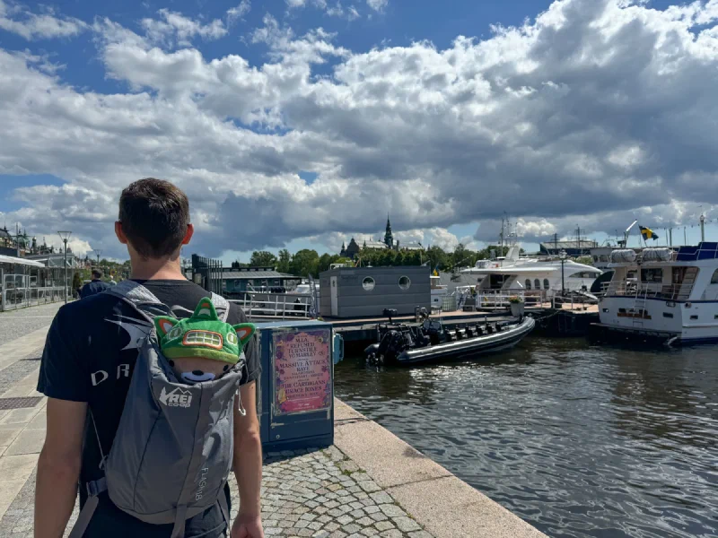 Nicholas walking along harbor with Sumi peeking from backpack