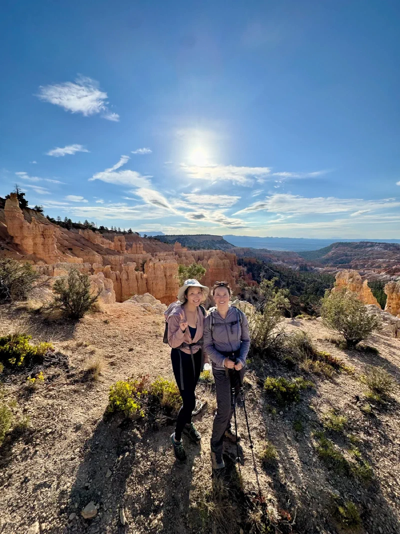 Two hikers on the rim with hoodoos behind