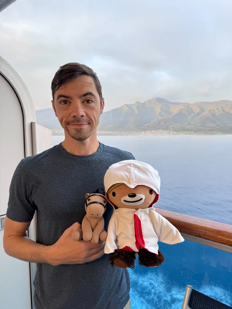 Nicholas on cruise ship balcony holding Sumi and Chestnut with dramatic green Maui mountains in background