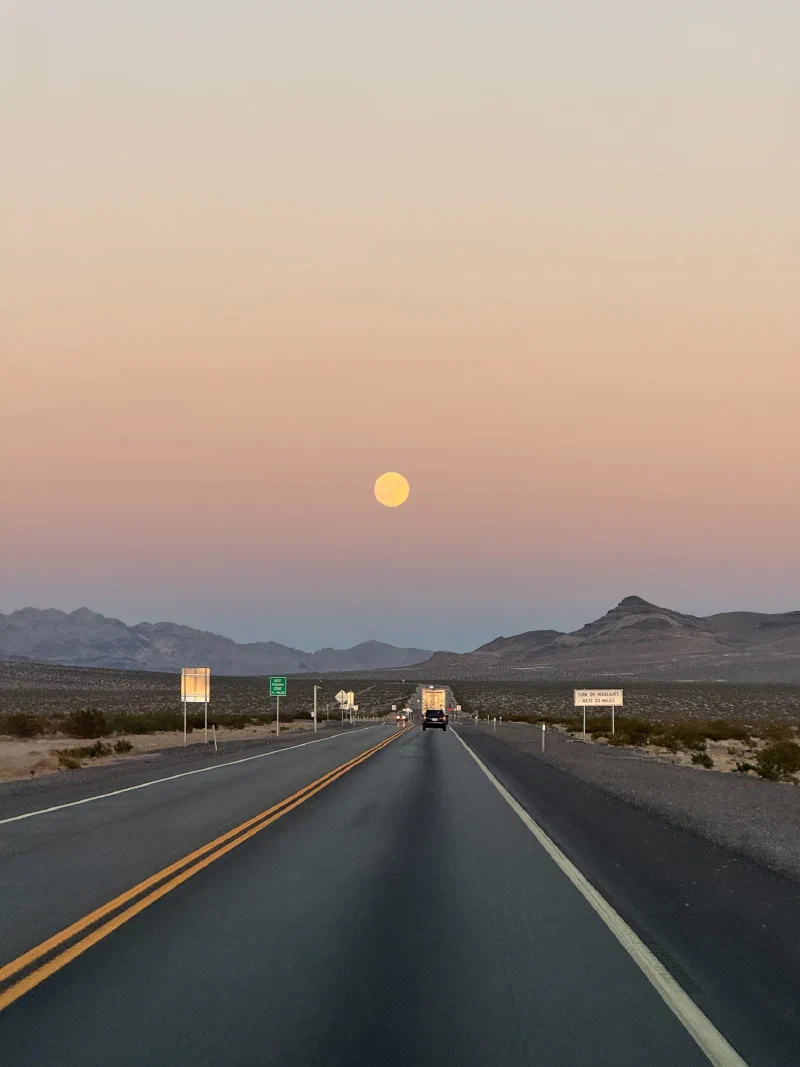 Full moon rising over a straight desert highway at dusk