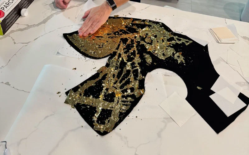 Hands pressing gold leaf onto black costume fabric
