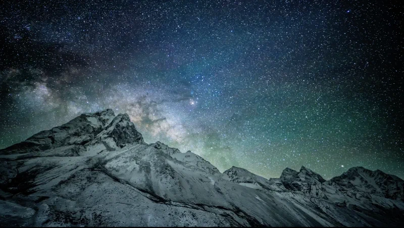 The first frame of a Milky Way timelapse near Dingboche, with the dust band emerging from behind a snow-covered Ama Dablam peak and the galactic core still hidden behind the mountain, green airglow along the horizon