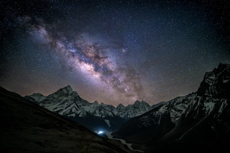 The Milky Way over a snow-capped triangular peak at Thukla, with a winding valley path leading toward distant village lights