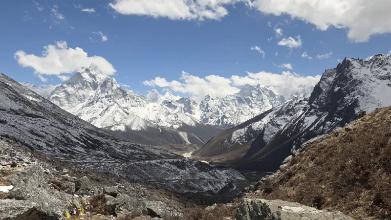Panoramic daytime view from the Sherpa Memorial near Lobuche, showing a glacial valley ringed by snow-covered Himalayan peaks under a deep blue sky
