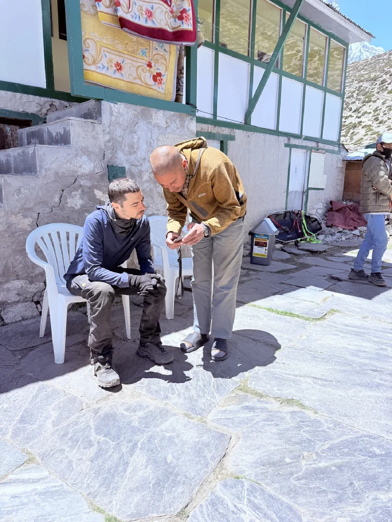 Nicholas sitting exhausted at a lodge while another man shows him something on a phone
