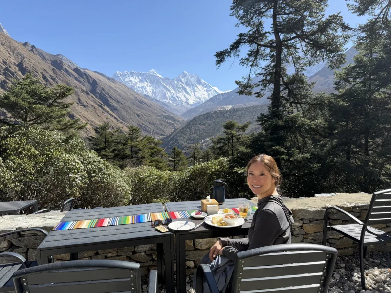 Pokin sitting at an outdoor terrace table with a full breakfast spread and snow-capped Himalayan peaks in the background