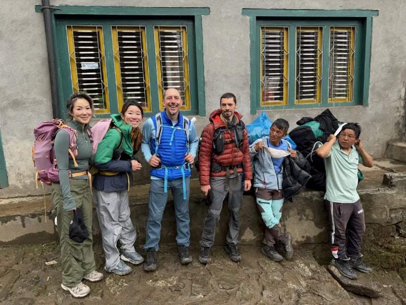 The group posing in trekking gear outside a concrete trail hut