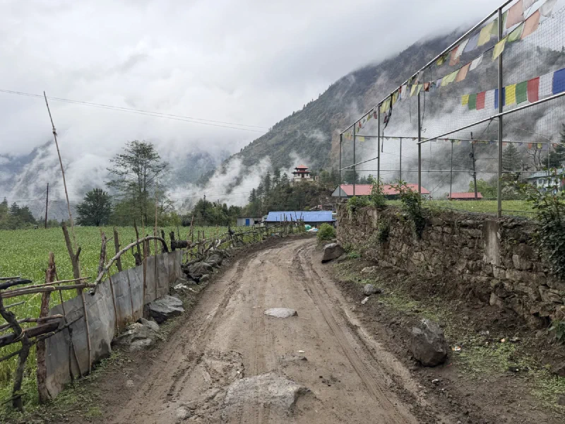 Approaching Surke village on a muddy road, prayer flags and a monastery on a misty hill