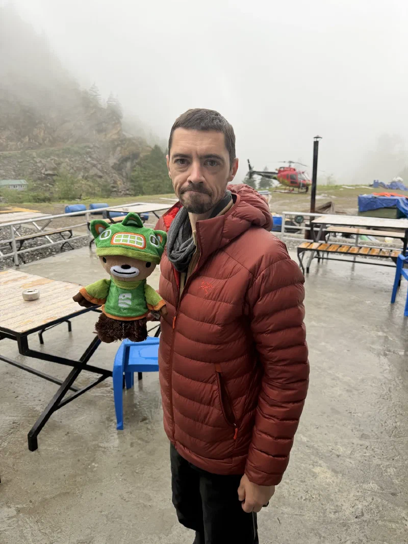 Nicholas holding Sumi the bear with a fogged-in red helicopter behind them at the helipad