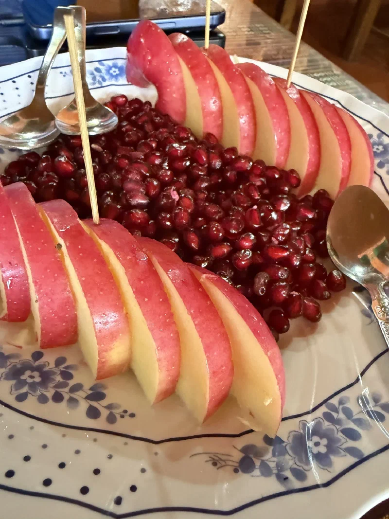 Plate of sliced apples and pomegranate seeds with wooden skewers