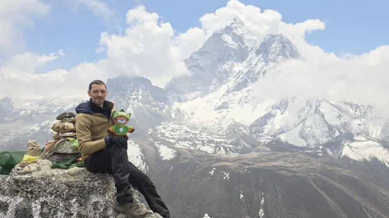 Nicholas sitting with Sumi at a cairn with prayer flags and Ama Dablam behind