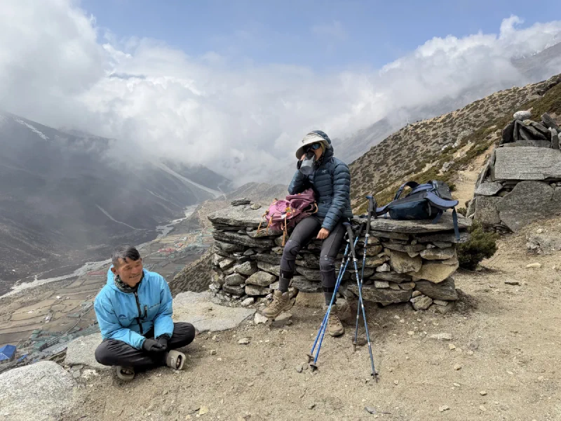 Two people resting on trail overlooking Dingboche village