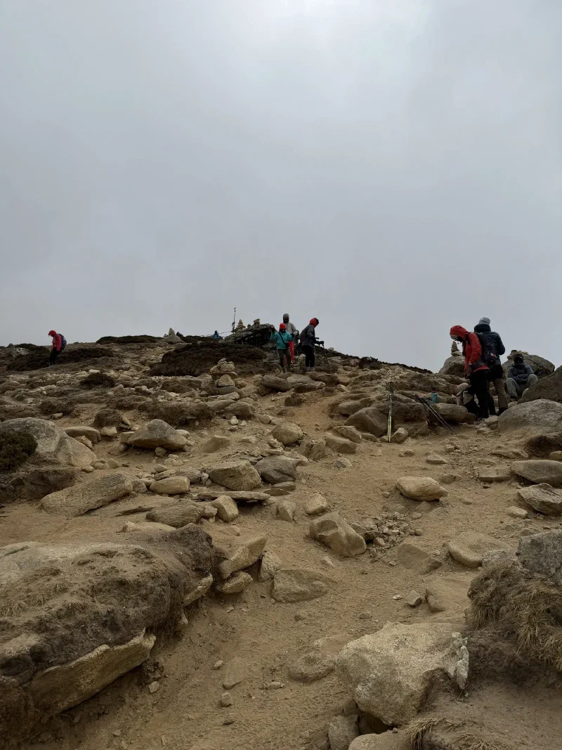 Trekkers climbing steep rocky slope with cairns at the top