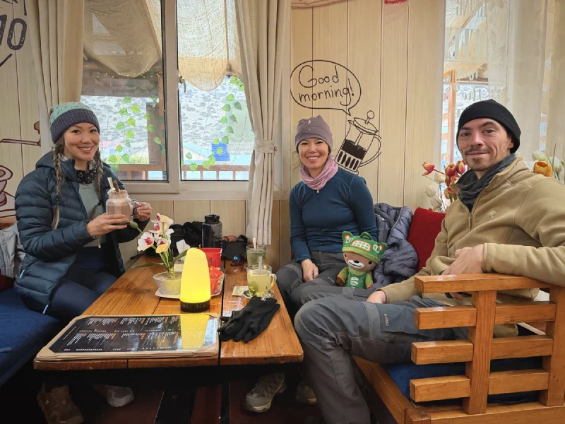 Three trekkers relaxing at a cafe table with warm drinks