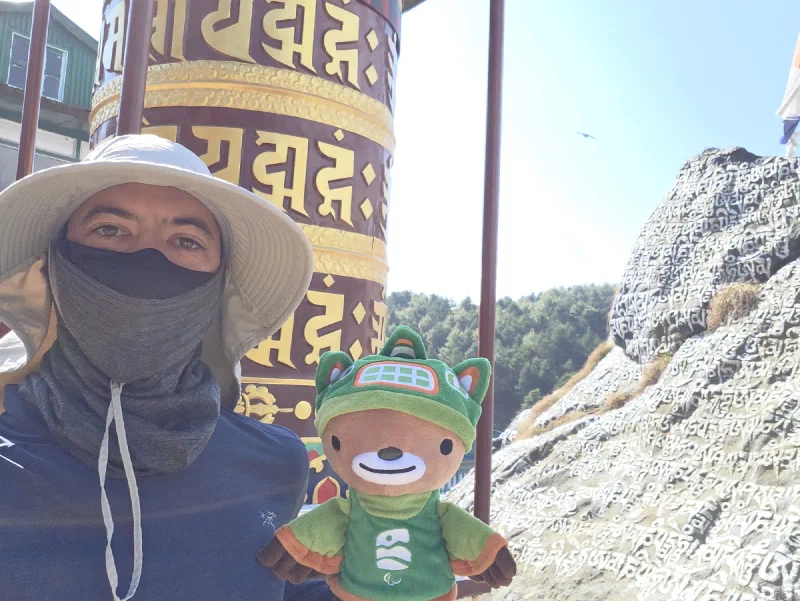 Nicholas holding Sumi Bear next to large prayer wheel and mani wall