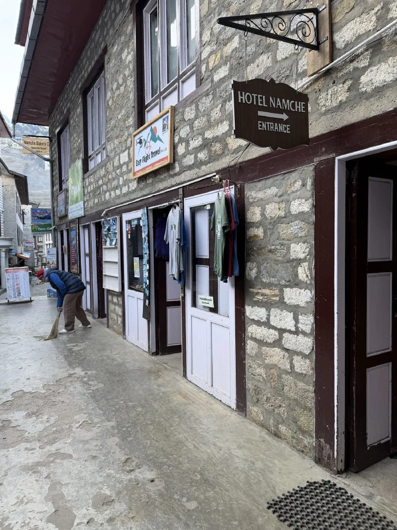 Narrow Namche street with Hotel Namche sign and person sweeping in early morning