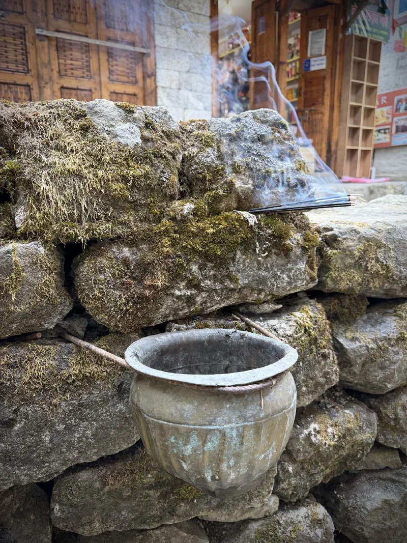 Incense burning in moss-covered stone wall with oxidized copper pot