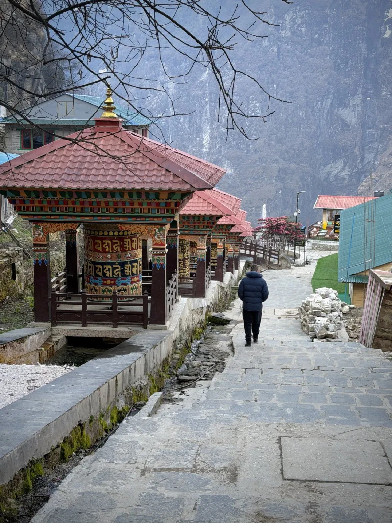 Row of ornate prayer wheels along stone path with lone trekker