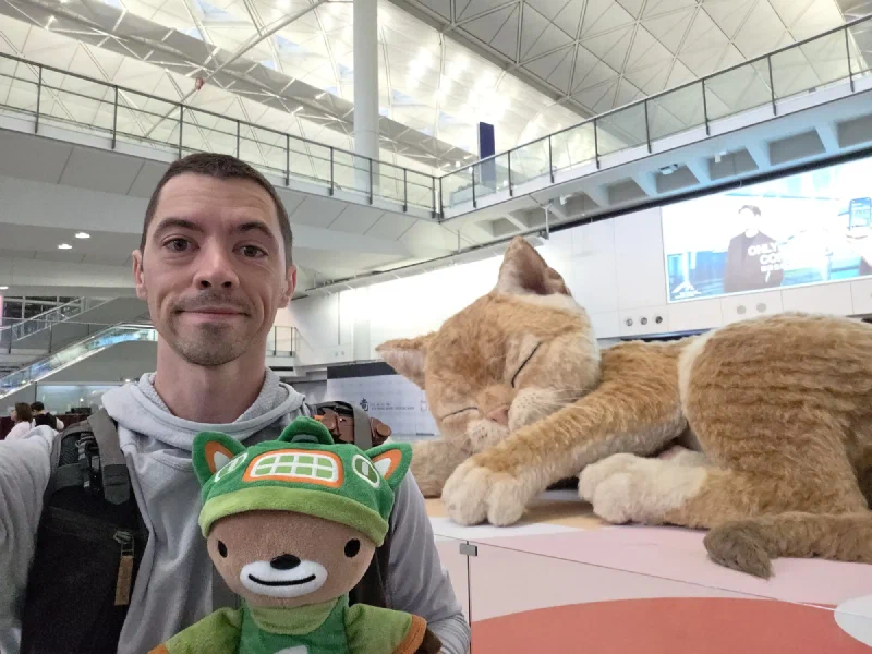 Nicholas and Sumi in front of a giant sleeping cat sculpture at Hong Kong airport