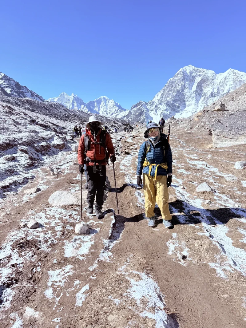 Nicholas and Alice hiking the trail with snow-covered peaks behind