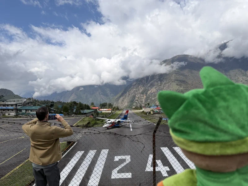 A small plane on the Lukla Airport runway with cloud-covered mountains behind