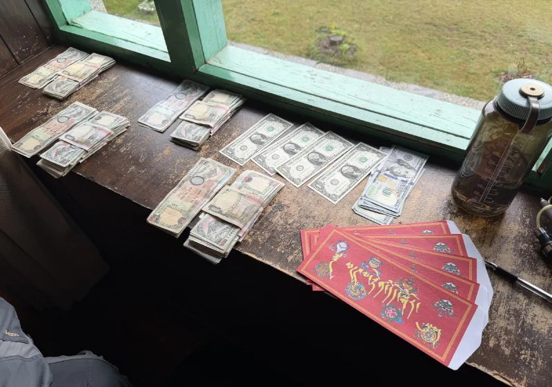 Stacks of Nepalese rupees and US dollars on a windowsill next to red envelopes