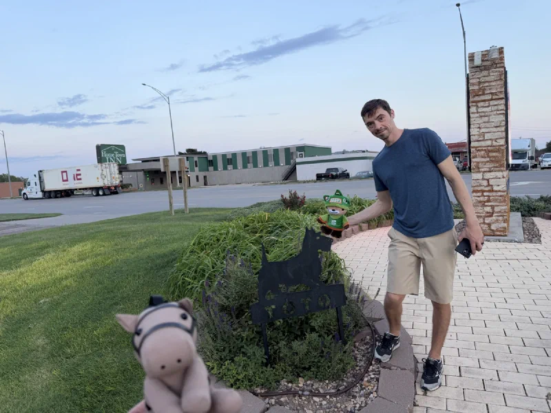 A black metal silhouette of a dog with TOTO cut into the base, with a motel sign and a parked semi-truck across the street behind it