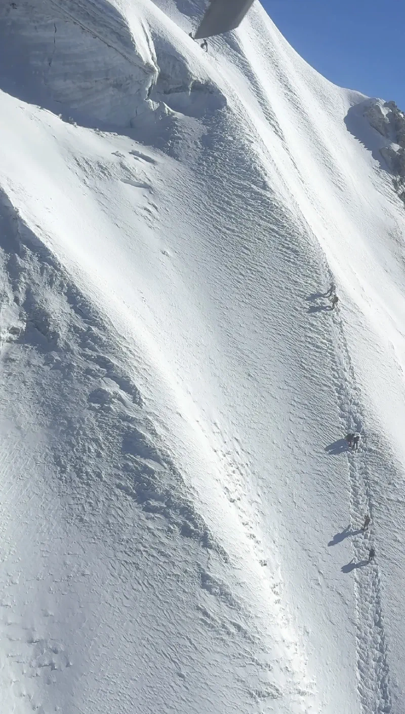 Climbers ascending a steep snow slope on Lobuche Peak, seen from a helicopter