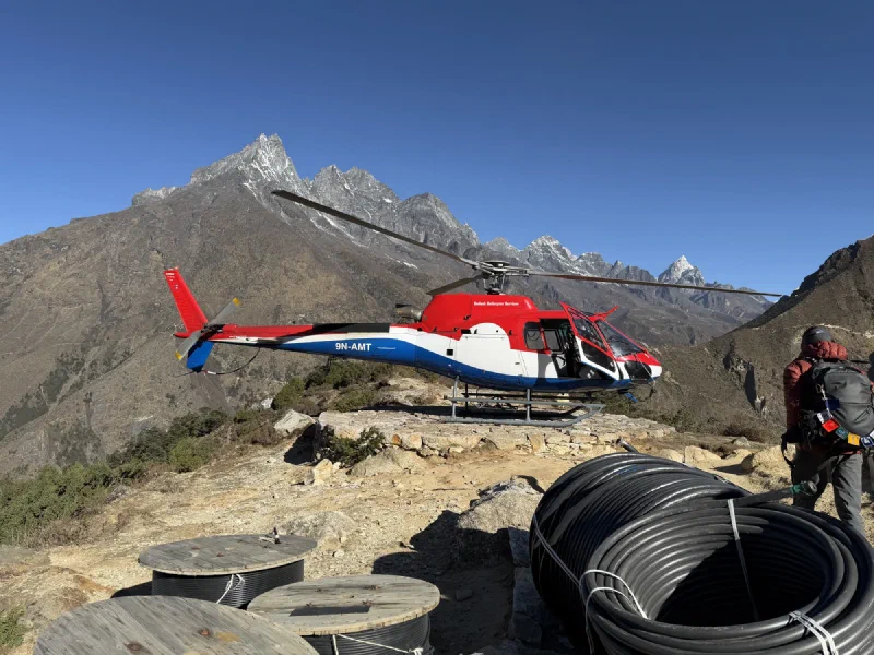 Red white and blue helicopter parked on a rocky mountain helipad with dramatic Himalayan peaks behind