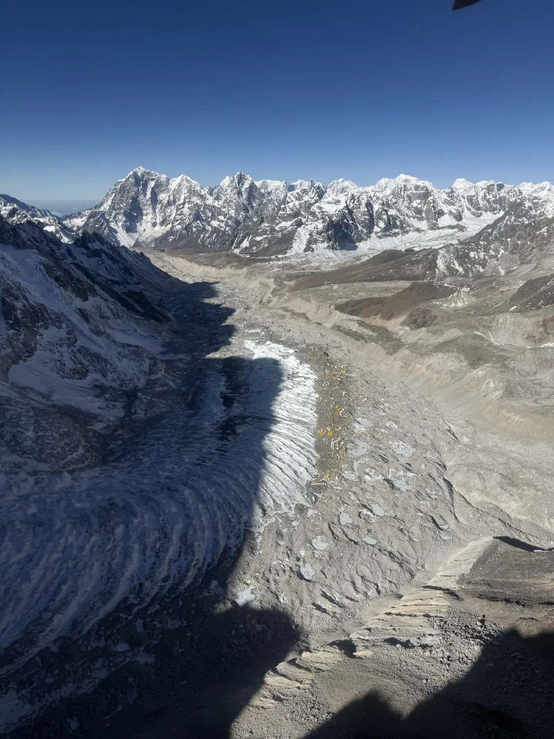 Aerial view of the Khumbu Glacier and Everest Base Camp tents from helicopter, with the helicopter shadow visible on the moraine