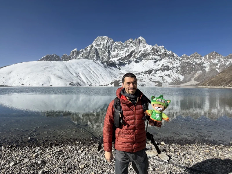 Nicholas holding Sumi at Gokyo Lake with snow-capped mountains perfectly reflected in the still water