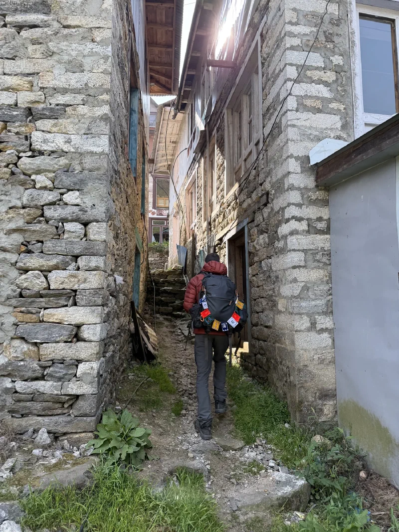 A trekker walking through a narrow stone alley between buildings in Phakding